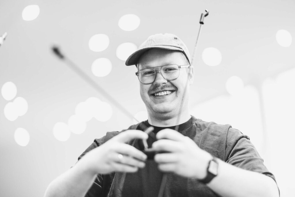 Person mit Kappe laechelt und haelt einen Gegenstand in den Haenden.