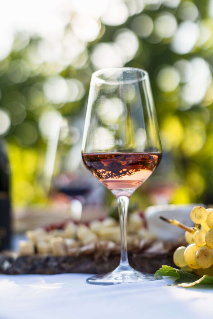 Ein Glas Rotwein auf einem Tisch im Freien mit Trauben im Hintergrund.