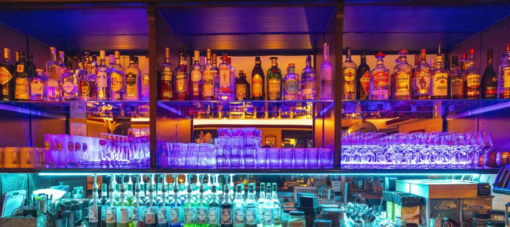 Eine bunte Bar mit lebhaften Lichtern und Regalen voller Flaschen.