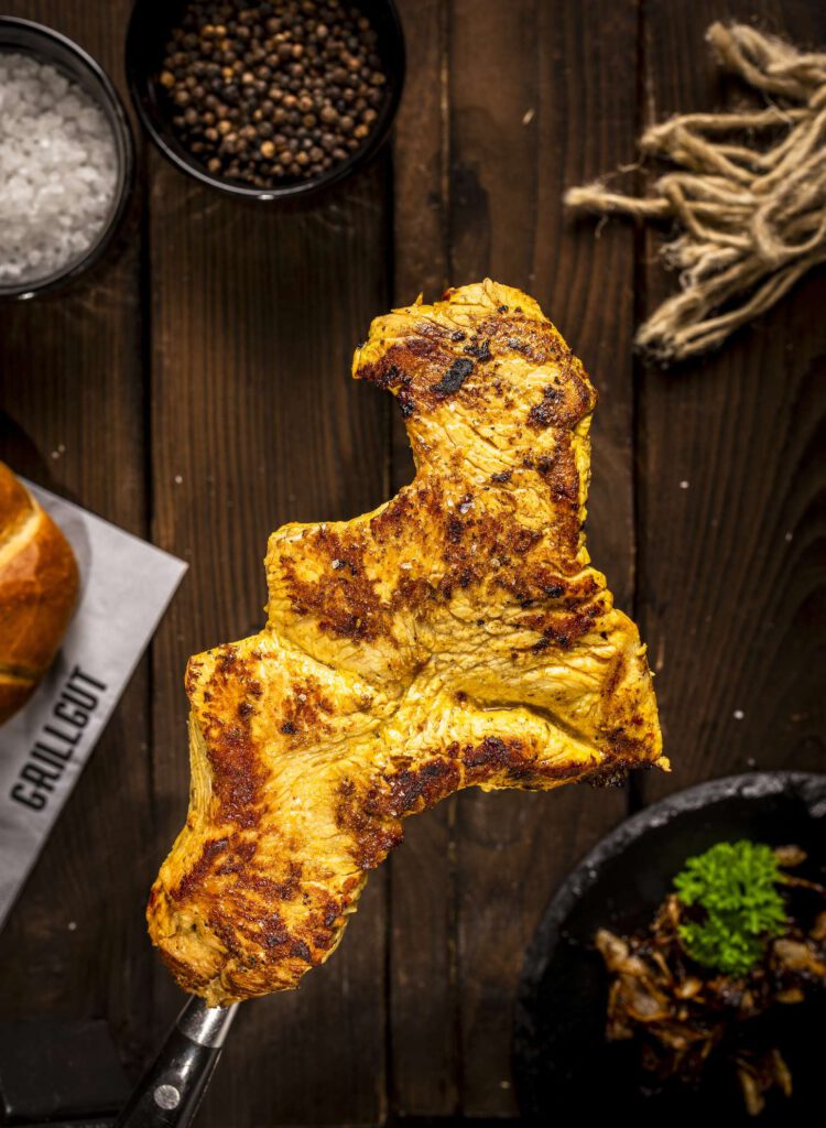 Gegrillter Haehnchenspieß auf Holztisch mit Beilagen.