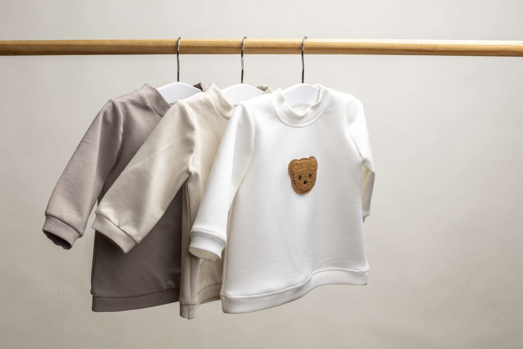 Drei Kinderoveralls in verschiedenen Farben haengen an einem Kleiderbuegel.