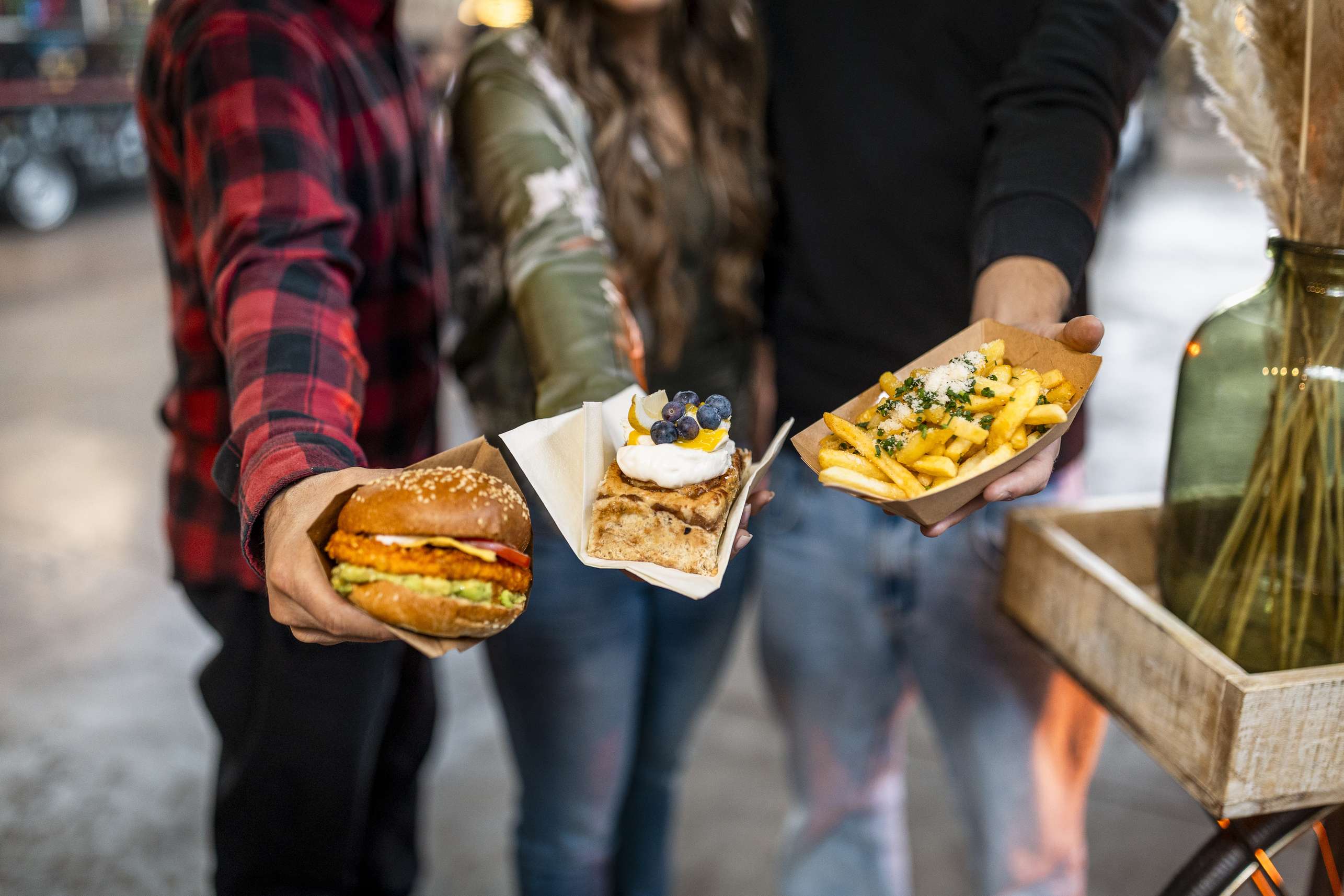 Drei Personen halten Burger und Desserts von verschiedenen Foodtrucks.