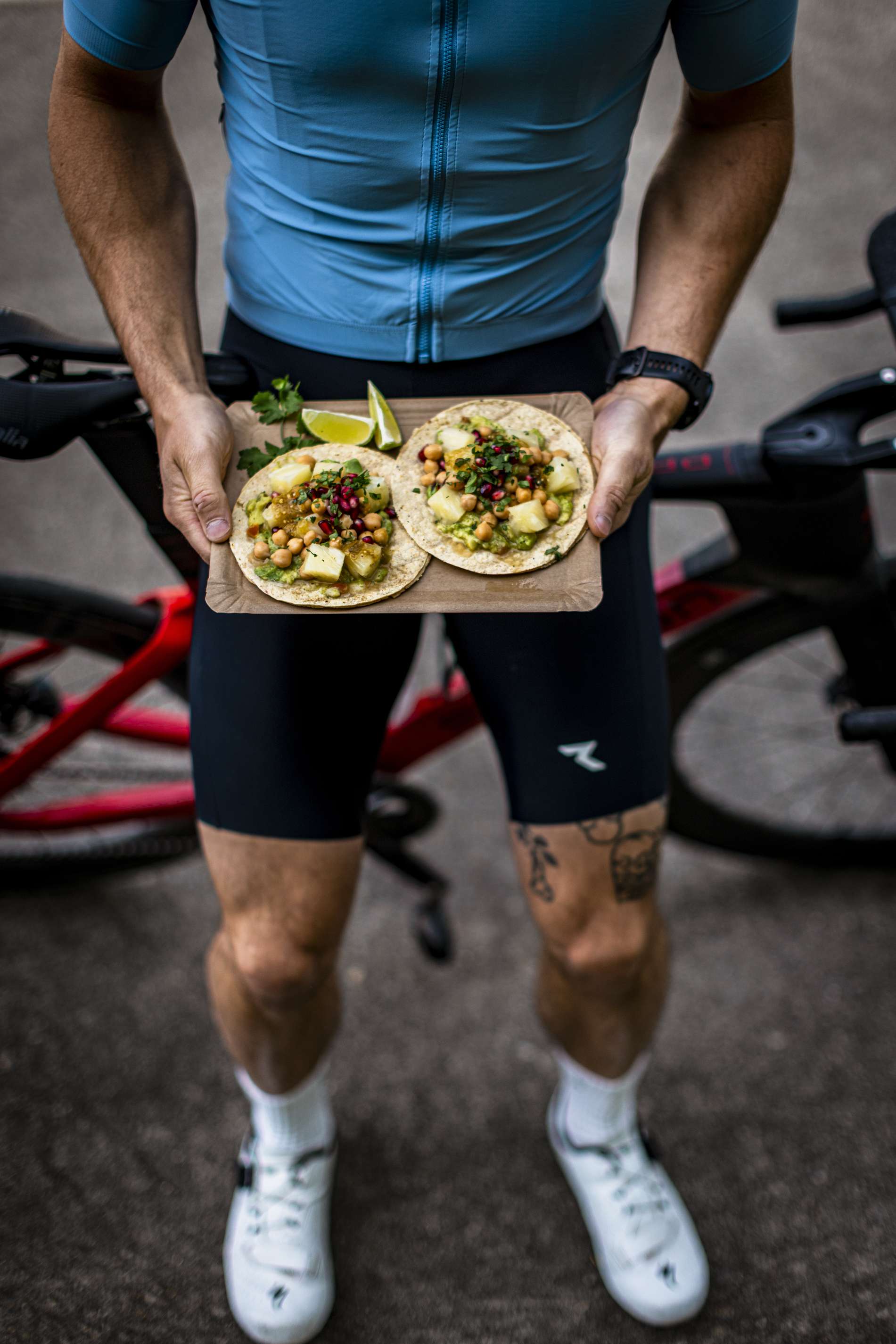 Ein Mann in Fahrradkleidung haelt eine Platte mit Tacos.