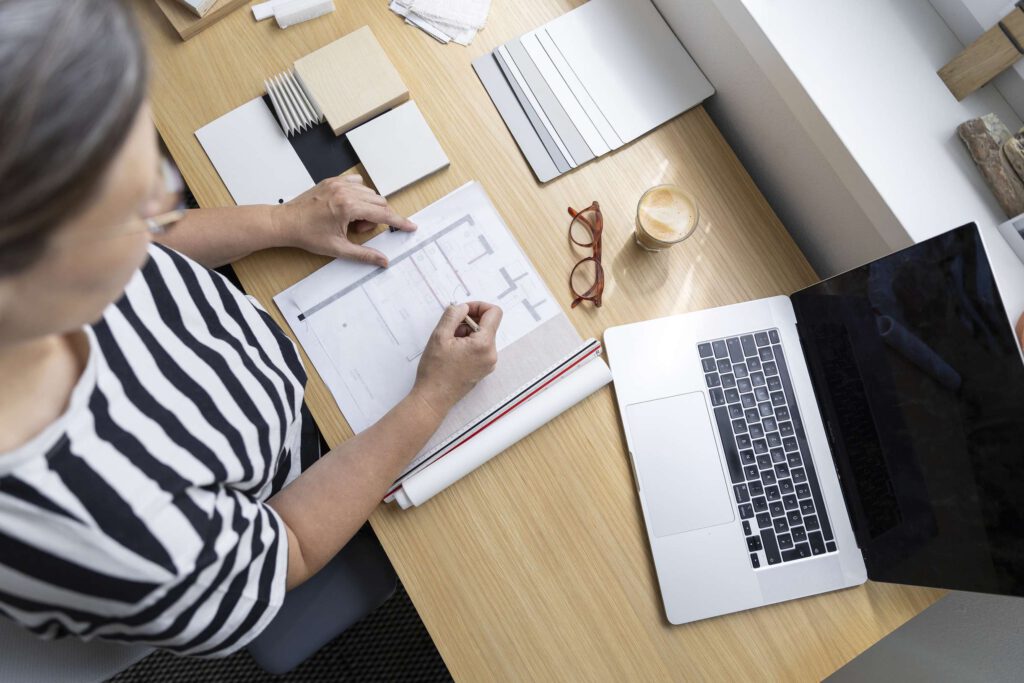 Frau macht Notizen an einem Schreibtisch mit Laptop und Schreibmaterialien.