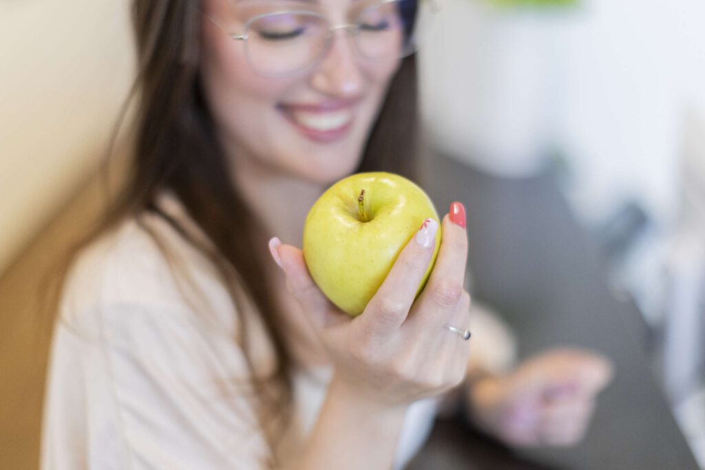 Frau laechelt und haelt einen Apfel in einer Zahnarztpraxis in Albstadt.