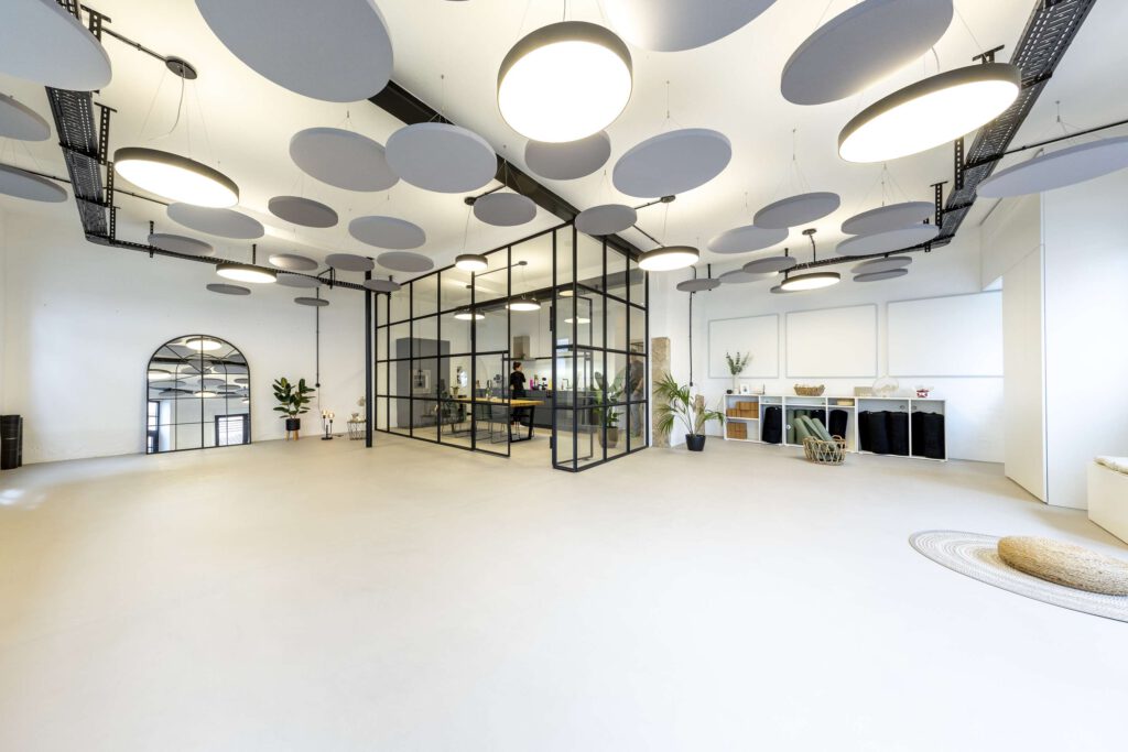 Ein moderner Bueroraum mit offenen Arbeitsplaetzen, großen Deckenleuchten und stilvollen Designelementen.