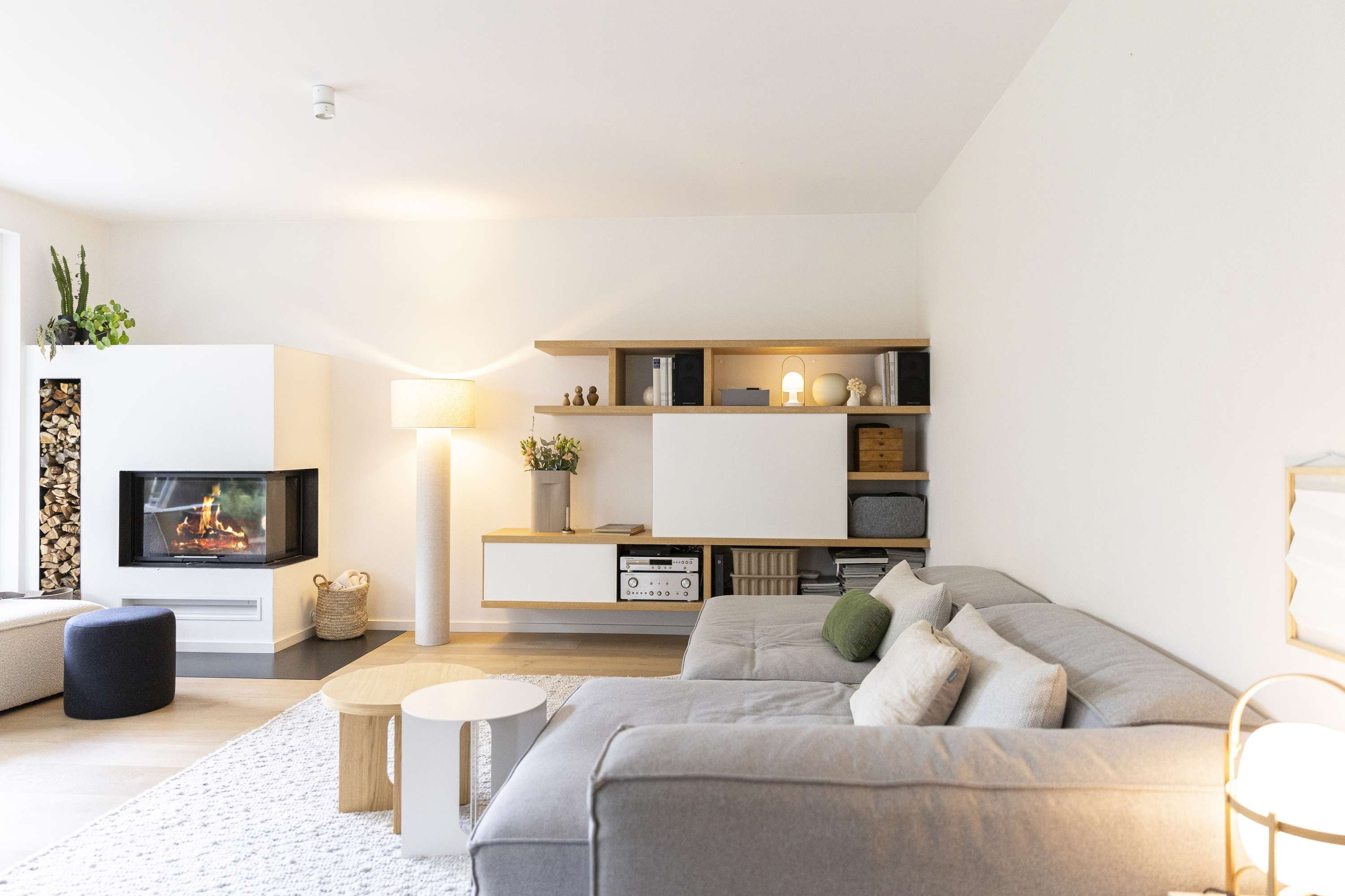 Gemuetliches modernes Wohnzimmer mit grauem Sofa und Kamin in hellen Farben