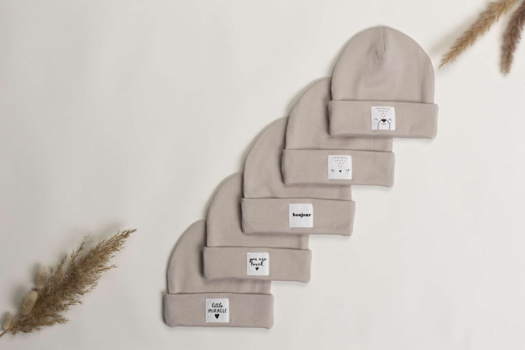 Fuenf beige Muetzen in einer Reihe auf einer hellen Oberflaeche mit dekorativen Federn im Hintergrund.