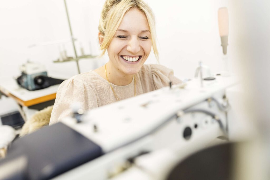Eine Frau naeht laechelnd an einer Naehmaschine.