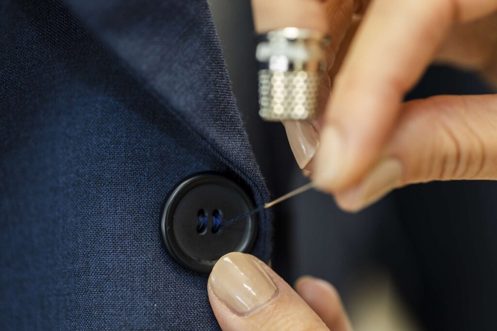 Eine Person naeht einen Knopf an eine blaue Jacke an.