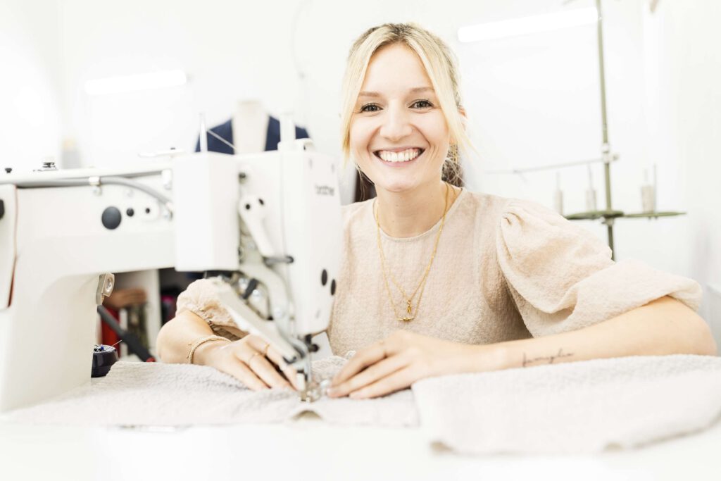 Frau sitzt laechelnd an einer Naehmaschine.