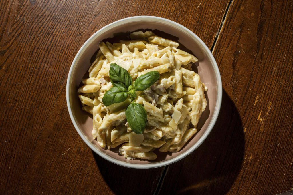 Eine Schuessel mit Pasta, garniert mit Basilikum auf einem Holztisch.