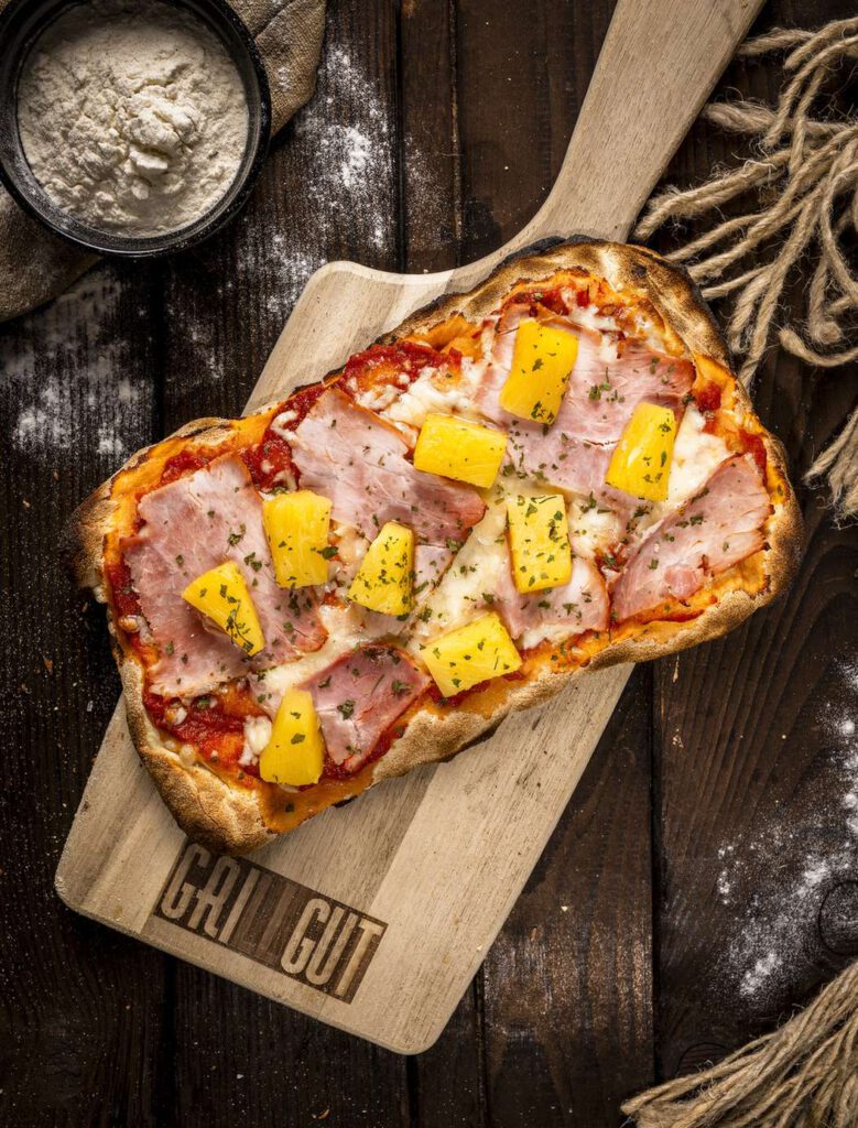Ein Pizza-Toast mit Schinken und Ananas auf einem Holzbrett.