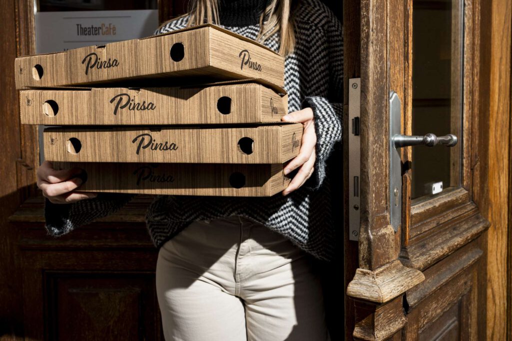 Person traegt drei Pizzaschachteln durch eine Tuer