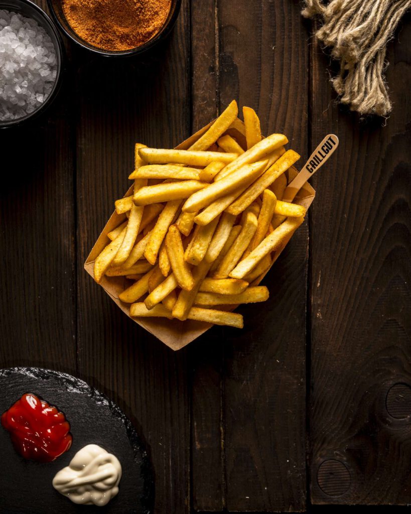 Pommes Frites serviert mit Auswahl an Saucen auf dunklem Holztisch.