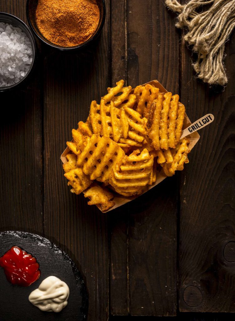 Waffle-Pommes-frites mit Dips auf einem rustikalen Tisch.