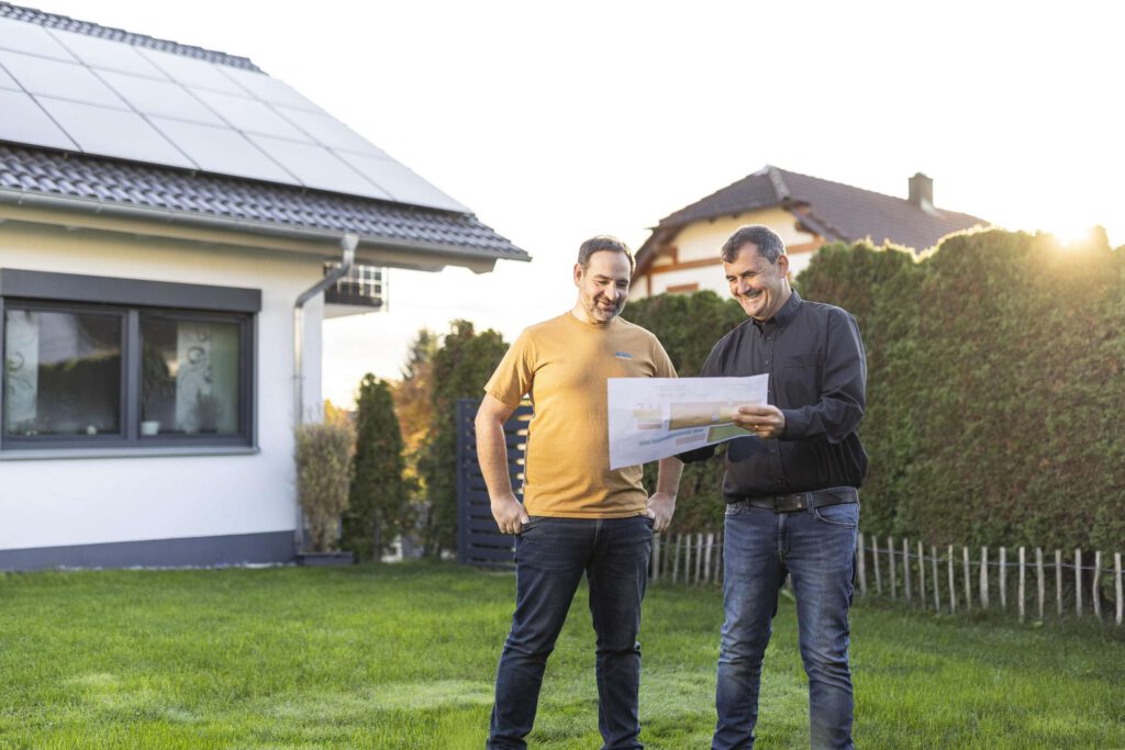 Zwei Personen planen eine Photovoltaik-Installation vor einem Haus.
