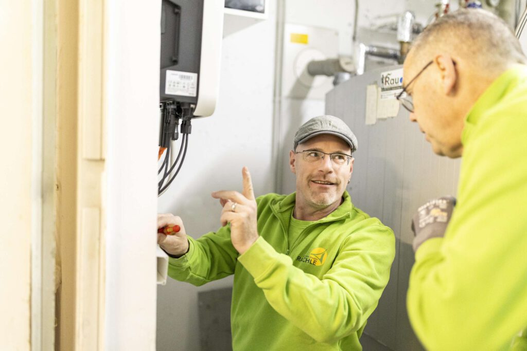 Zwei Handwerker in gruener Kleidung arbeiten an einer Photovoltaik-Installation.