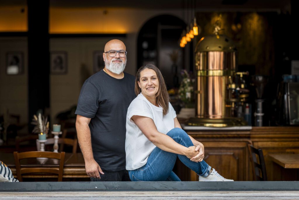 Ein Mann und eine Frau posieren laechelnd vor der Theke eines Restaurants.