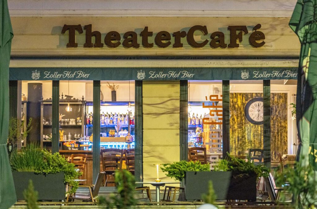 Außenansicht eines Theatercafés mit beleuchtetem Innenraum und Ladenfront.