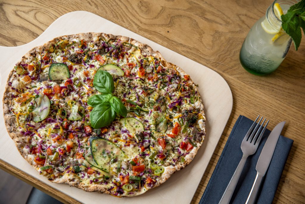 Vegetarische Pizza auf einem Holzbrett serviert mit Gabel und Messer.