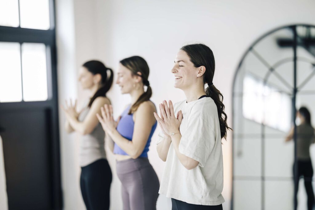 Drei Frauen praktizieren Yoga in einem Studio mit großen Fenstern.