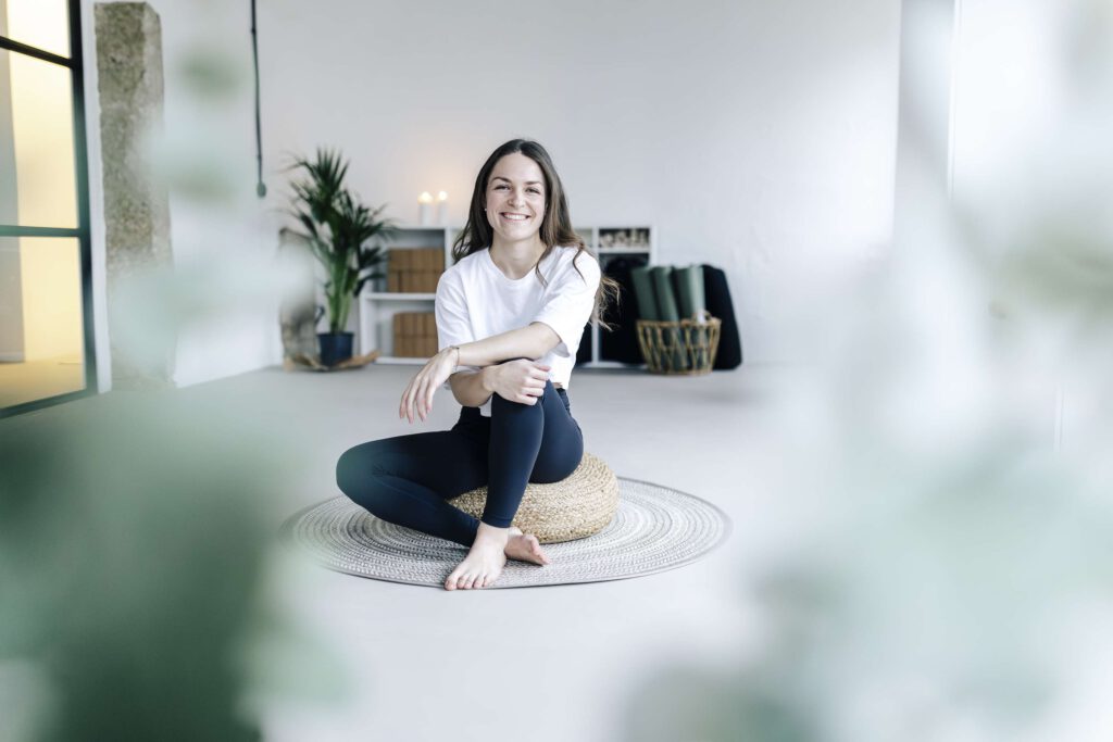Frau sitzt in einem hellen Raum im Schneidersitz und meditiert.